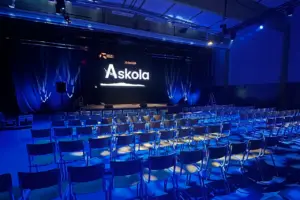 Seminaarisali, joka on valaistu siniseksi. Siistit penkkirivit etualalla ja takalalla lavalla on yrityksen logo screenillä